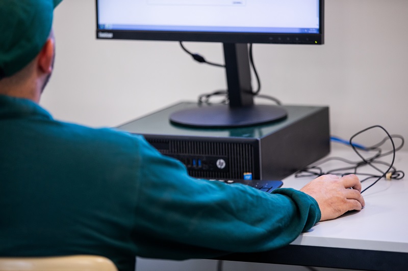 A man sitting infront of a desktop, holding the mouse. There is a keyboard too.