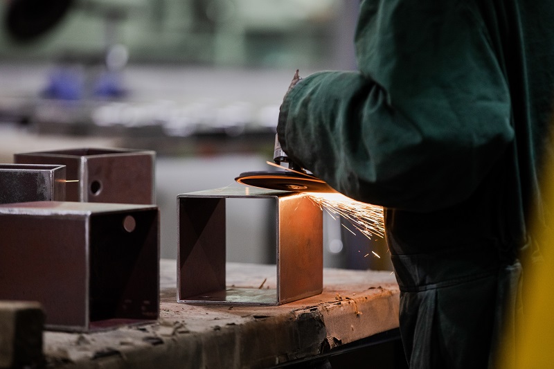 Person using an angle grinder on a piece of metal with orange sparks