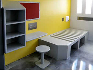 Cell furniture, one bed, one round table secured to the ground,  one table attached to the wall, one shelf with three compartments, one bown wall board.
