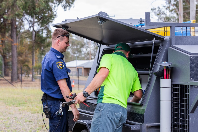 Two people grabbing tools from a work vehicle