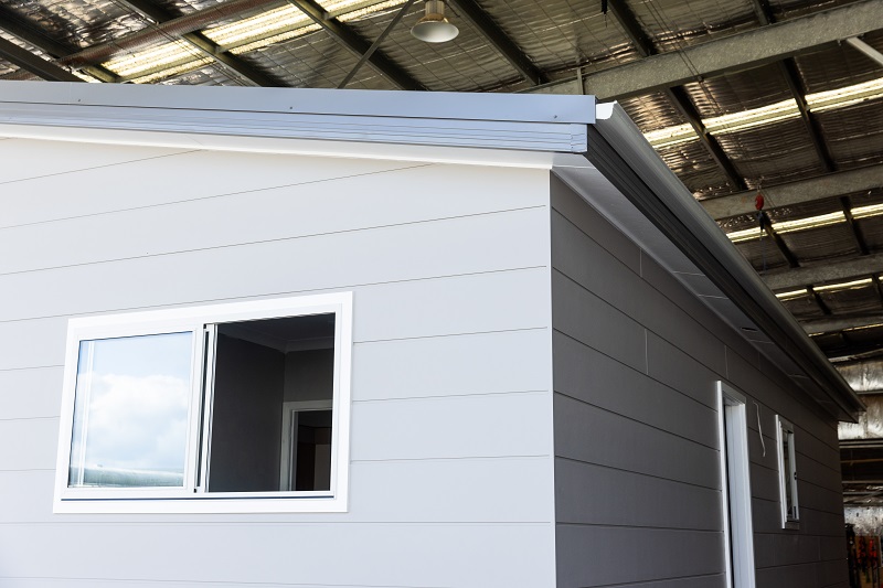 External modular building with cladding and metal roof / gutter stored in a large warehouse