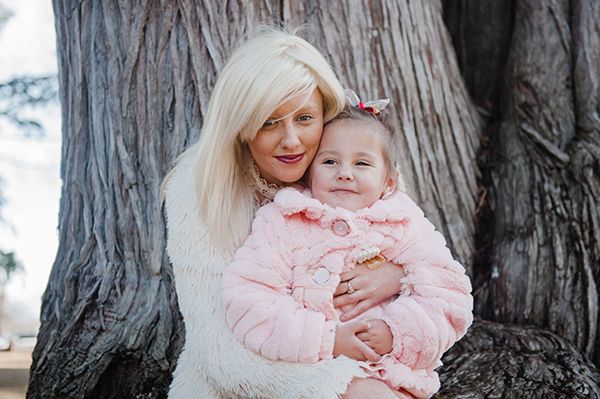 A blond haired adult female hugging a young girl both smiling and happy