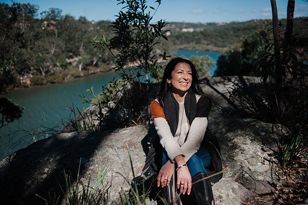 A middle ages female with black hair sitting and smiling next to a river