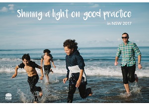 Three children running on a beach happy whilst their father is watching over them. 